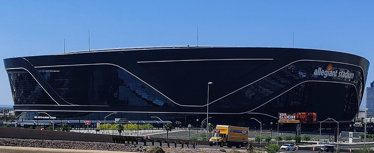 The sleek black, fully enclosed Allegiant Stadium under a clear blue sky in Las Vegas, with a delivery truck driving past in front.