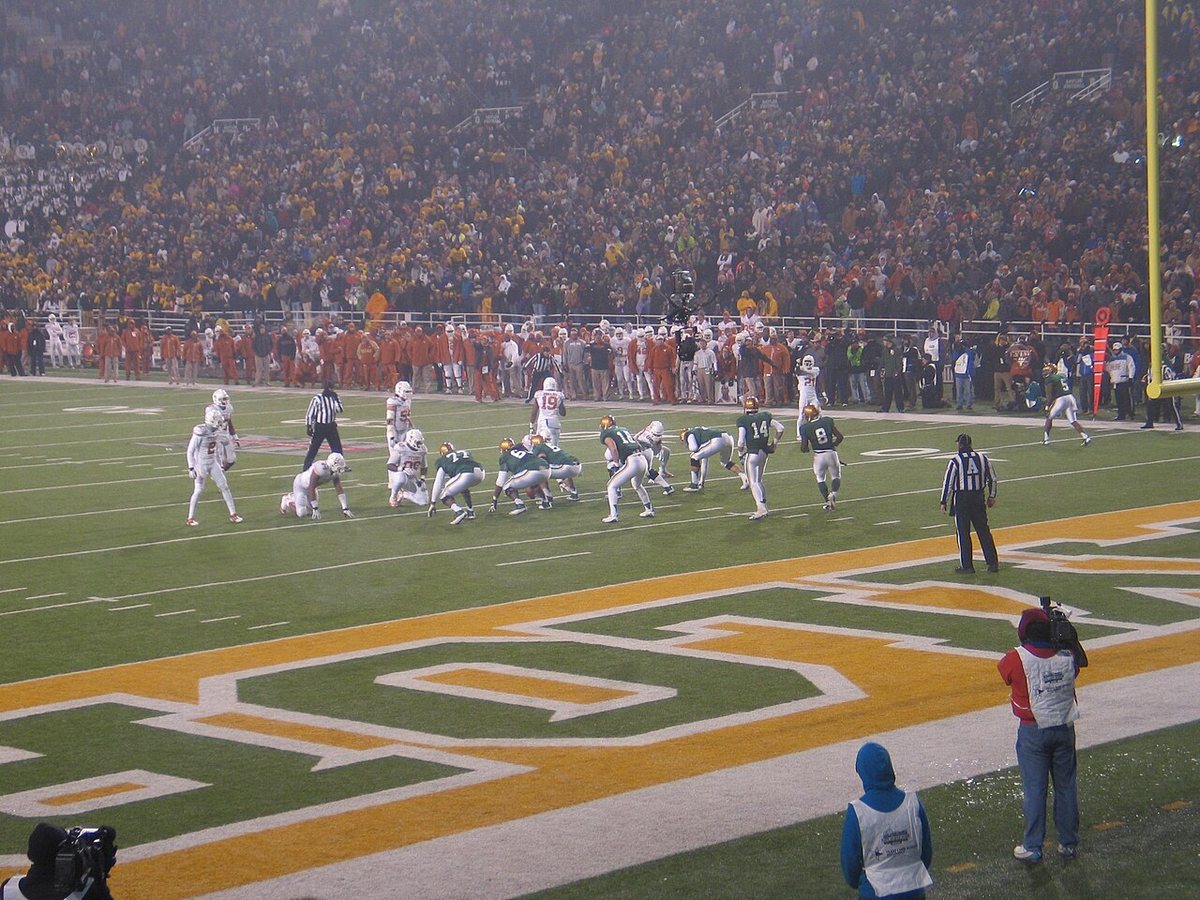 Baylor players in green lined up at the line of scrimmage against Texas players in white, in front of a packed, misty stadium with the Baylor logo painted in the end zone.