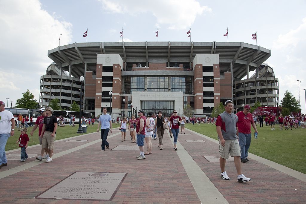 Fans in crimson walk away from Bryant-Denny Stadium at the University of Alabama on a sunny day.