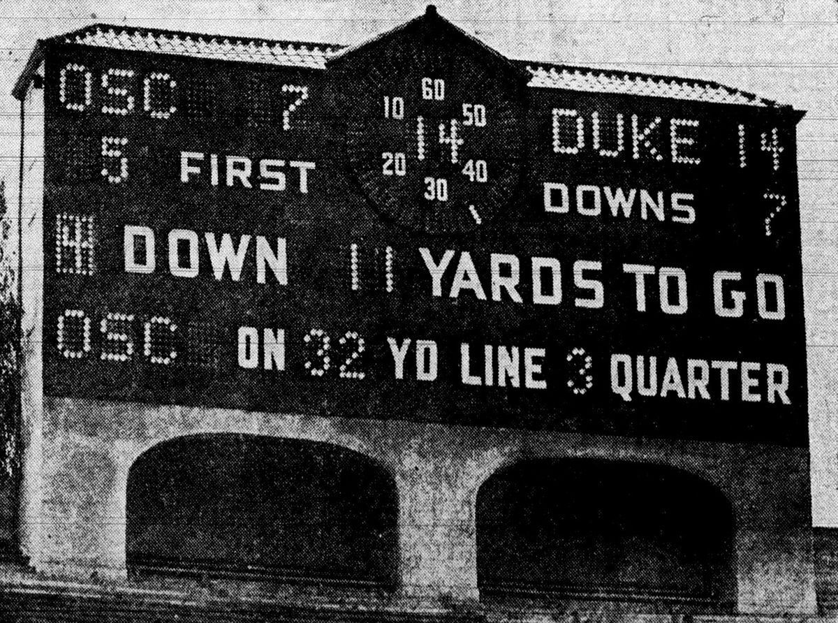 A black-and-white photo of an old stadium scoreboard showing the score, down, yards to go and quarter.