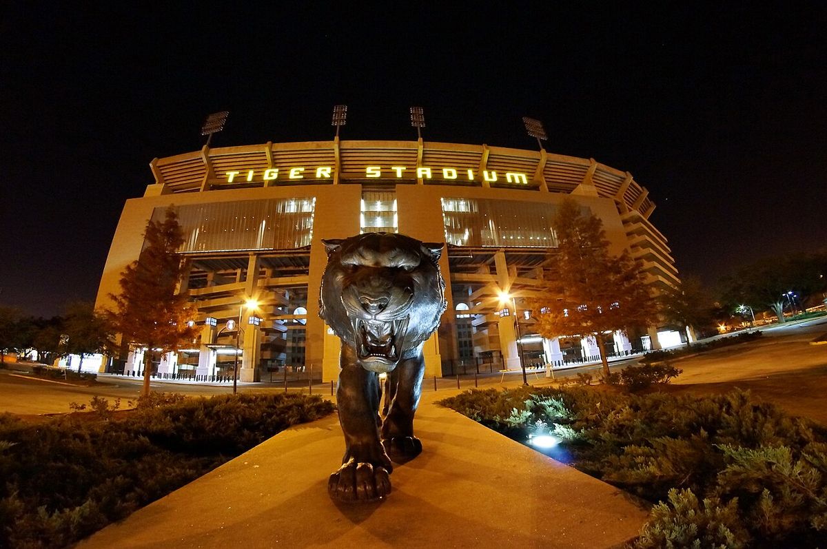 A bronze tiger statue in front of LSU's Tiger Stadium, lit up at night.