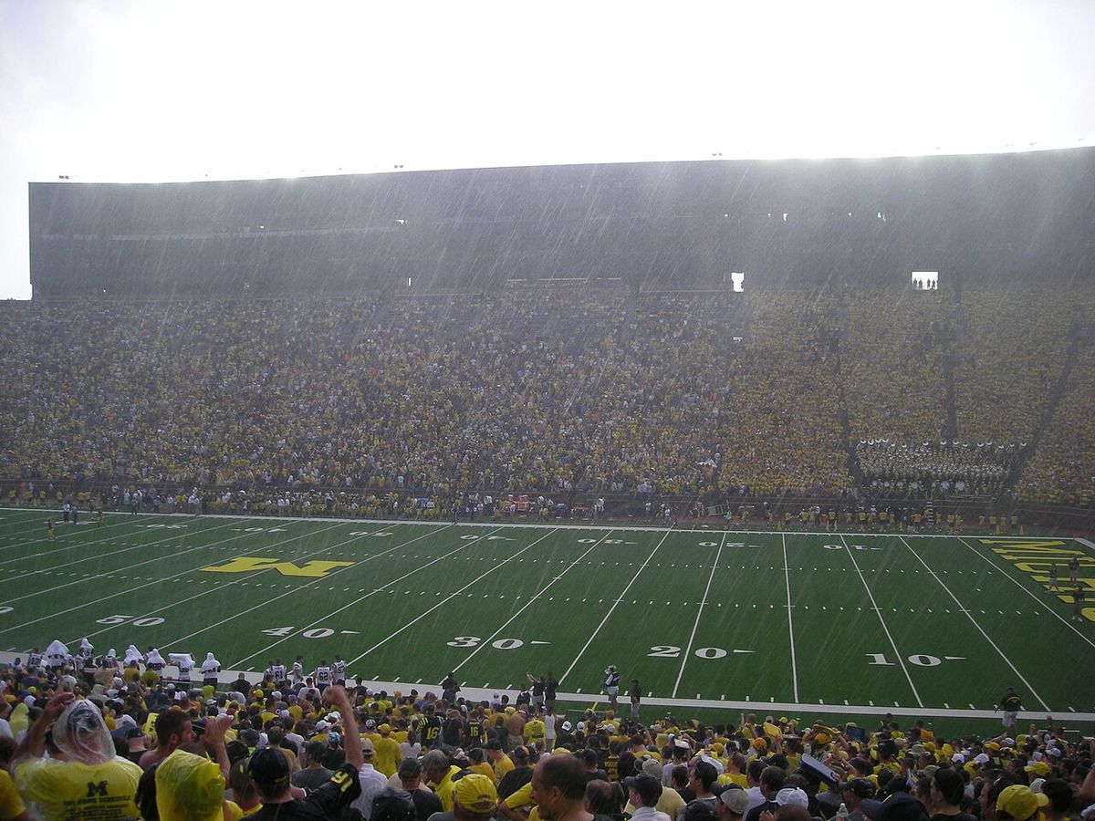 Heavy rain falling over a packed Michigan Stadium, seen from high in the stands.