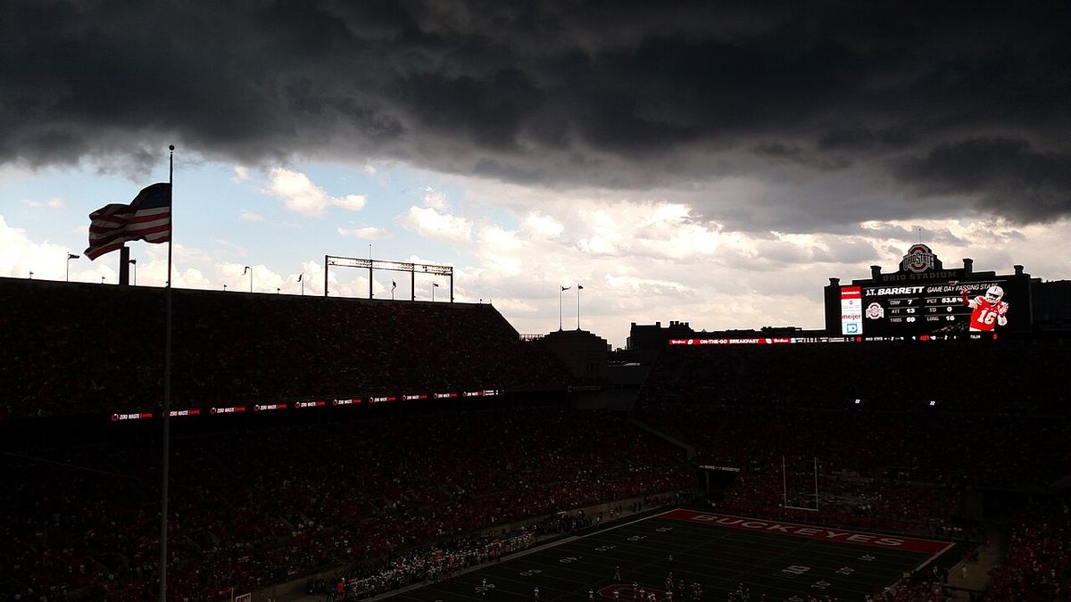 Huge dark storm clouds loom over Ohio Stadium during a game, with the stands in shadow.